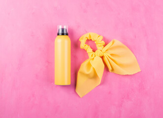Yellow sun protection spray and romantic hair tie with bow over pink textured background. Summer in the city or in vacation. Flat lay