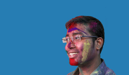 side portrait of a young man with holi colours on face smiling a with isolated solid sky background