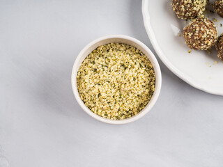 Shelled hemp seeds superfood in white bowl over gray background as ingredient of energy protein balls. Top view