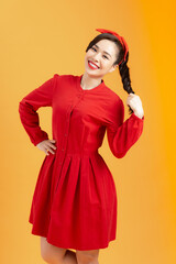 Portrait of a cheerful young Asian woman in red dress posing and looking away over orange background