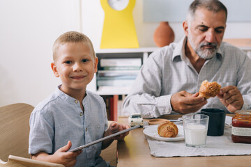 grandfather and grandson using tablet computer while having breakfast at home