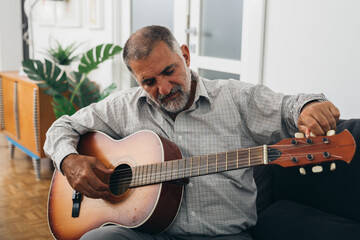 senior bearded man playing guitar at his home