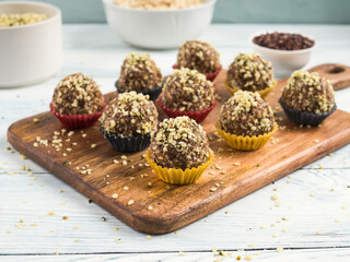 Home made vegan energy protein balls with oats, nuts, dates, dried fruit, flax and hemp seeds, chocolate nibs and maple syrup served in paper cases on wooden board.
