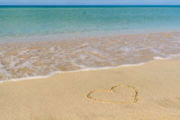 Heart drawing on the sandy beach. Near the blue sea.