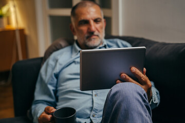 middle aged man sitting sofa using tablet computer at home