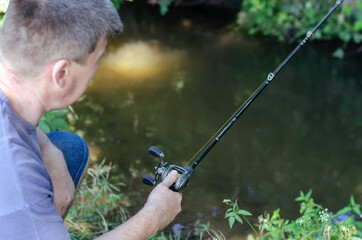 An adult man catches a predatory fish on the bank of a forest river.