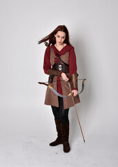 Full length portrait of girl with red hair wearing  brown medieval archer costume.. Standing pose...