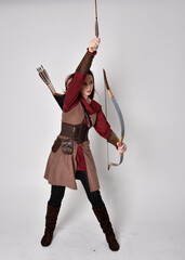 Full length portrait of girl with red hair wearing  brown medieval archer costume.. Standing pose...