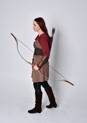 Full length portrait of girl with red hair wearing  brown medieval archer costume.. Standing pose...