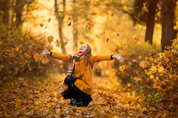 A girl in a yellow coat walks in an autumn park
