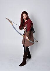 Full length portrait of girl with red hair wearing  brown medieval archer costume.. Standing pose...