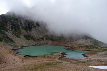 Alpine lake in the clouds. Alpine lake with rocky shores and emerald water in the clouds. Alpine lake Giybashkel (3240 meters above sea level), Caucasus. View from Yakov Pass.