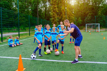 Kids in football uniform listening to explain of coach on training. Young coach explaining football game strategy to children soccer team.