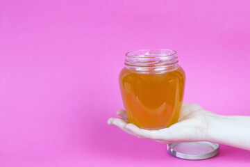 Glass jar with honey in a female hand on a pink background. Copy space - the concept of healthy eating, vitamins, health improvement, disease prevention, sweets