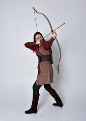 Full length portrait of girl with red hair wearing  brown medieval archer costume.. Standing pose...