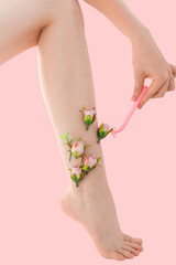 Obraz na płótnie Canvas Woman's thin unshaven leg with pink flowers on a pink background. Female shaves her leg with a pink razor. Feminism