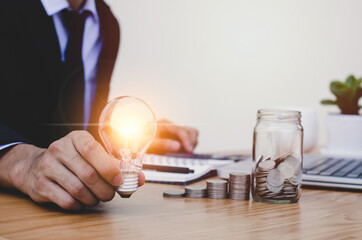 Businessman hand holding lightbulb and using a calculator to calculate accounting with saving money. concept of financial background