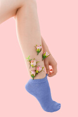 Woman's thin unshaven leg with pink flowers in the blue socks on a pink background. Feminism
