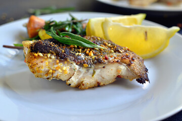 Grilled fish with lemon, herbs and rosemary. Fried fish fillets in a white plate. Beautiful presentation of food. Rucolla salad and carrots. Close-up.