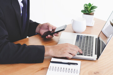 a young man working from home using a smart phone and laptop computer man. Side view shot of hands using a smartphone, the man at his workplace.
