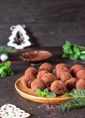 Dark chocolate truffles with raw cocoa powder, mint and fir tree branches, dark brown stone background. Christmas composition. 