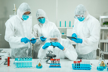 Group of Scientists wear Face Mask working in Lab while Checking Blood Sample by micro scope On Background.