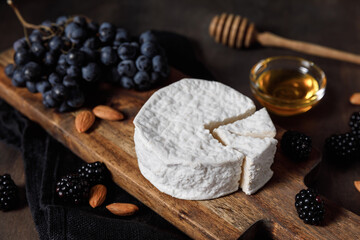 Camembert or brie french soft cheese with grapes, honey, nuts and berries on wooden background.