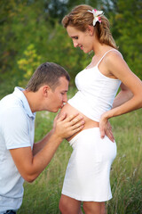 Obraz premium happy pregnant woman and her husband embracing her abdomen