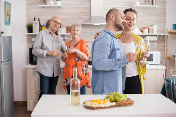 Happy couple with wine glasses in kitchen having a conversation. Appetizer with assorted cheese. Bottle of wine on table top.