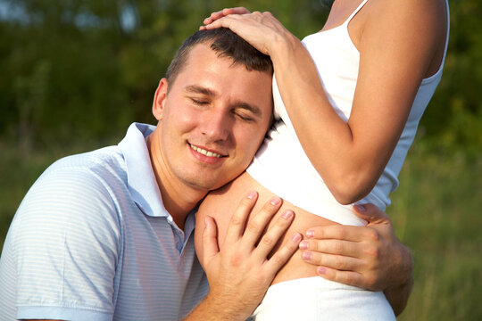 happy pregnant woman and her husband embracing her abdomen