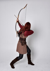 Full length portrait of girl with red hair wearing  brown medieval archer costume.. Standing pose...