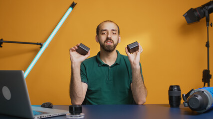 Vlogger recording review of li-ion batteries in studio. Videographer holding powerful accumulators....