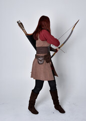 Full length portrait of girl with red hair wearing  brown medieval archer costume.. Standing pose...