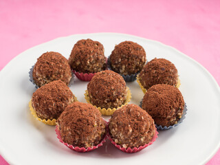 Home made vegan energy protein balls with oats, nuts, almond butter, dates, dried fruit, flax seeds, chocolate nibs on white dish on pink wooden background. Closeup