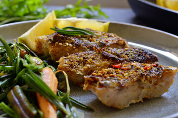 Grilled fish with lemon, herbs and rosemary. Fried fish fillets in a grey plate. Beautiful presentation of food. Rucolla salad and carrots. Close-up. Dark background