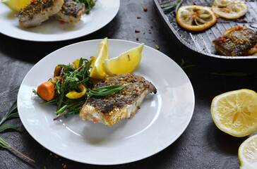 Grilled fish with lemon, herbs and rosemary. Fried fish fillets in a white plate. Beautiful presentation of food. Rucolla salad and carrots.