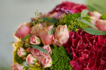Closeup bouquet of fresh pink roses, red hydrangeas, green throatwort on bright background. Blooming, spring, wedding or decoration concept.