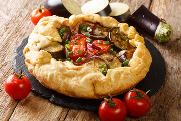 Freshly baked spicy eggplant galette pie with tomatoes, onions and herbs close-up on a slate board on the table. horizontal