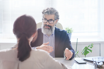 Modern mature man with beard on face discussing business project plan with woman sitting in front...