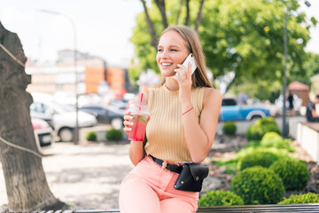 Young woman s talking phone holding mojito cocktail in the summer street