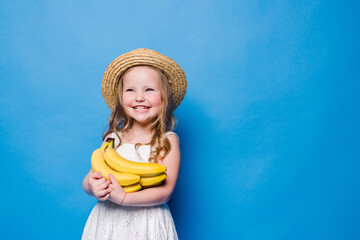 Happy little girl with yellow bananas isolated on blue background