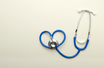 Top view of blue stethoscope in heart shape on the bright beige surface.Empty space