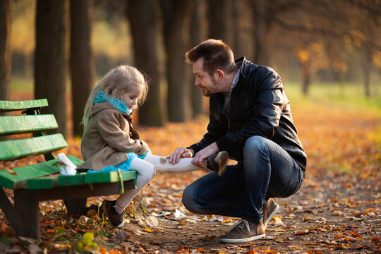 Dad cares of his little daughter after she fell down and hurted her knees in the autumn park. Father-daughter relationship, father's day, parental care.
