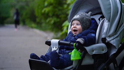 Little child in a stroller happy sits on the street walk the child in the park. beautiful blue eyed infant. baby carriage 