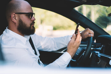 Businessman reading received smartphone notification while using self-driving in contemporary car...