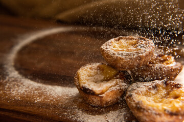 pastel di nata's getting sprinkled on a wooden board