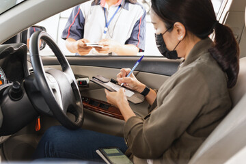 Woman with protective mask in car signing on transaction receipt with Credit Card for gasoline at gas station.