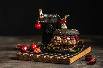 Black Burger with cherry sauce. Cheeseburger with black bun on dark background