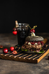 Black Burger with cherry sauce. Cheeseburger with black bun on dark background