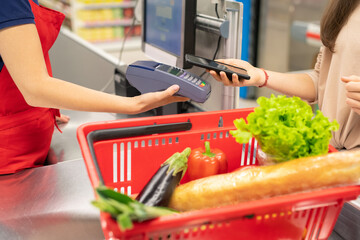 Unrecognizable young woman using NFC application on smartphone to pay for goods in modern store